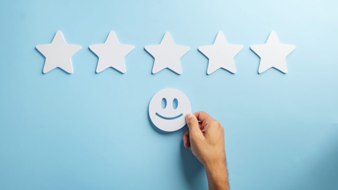 Feedback concept shows hand placing happy face beneath five white stars representing excellent customer satisfaction, positive service review experience for happy clients.
