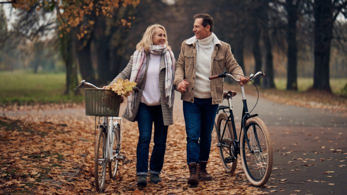 Senior couple walking in park in autumn. Attractive woman and handsome man spending time together with bicycles