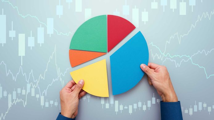 A person's hands holding a 3d pie chart over a background of line graphs